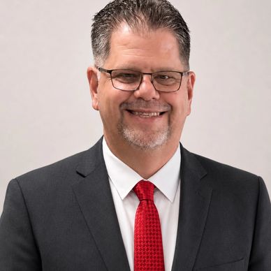 A smiling man in a black suit and red tie with glasses.