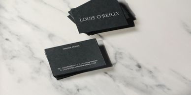 Black business cards for Louis O'Reilly on a marble surface.