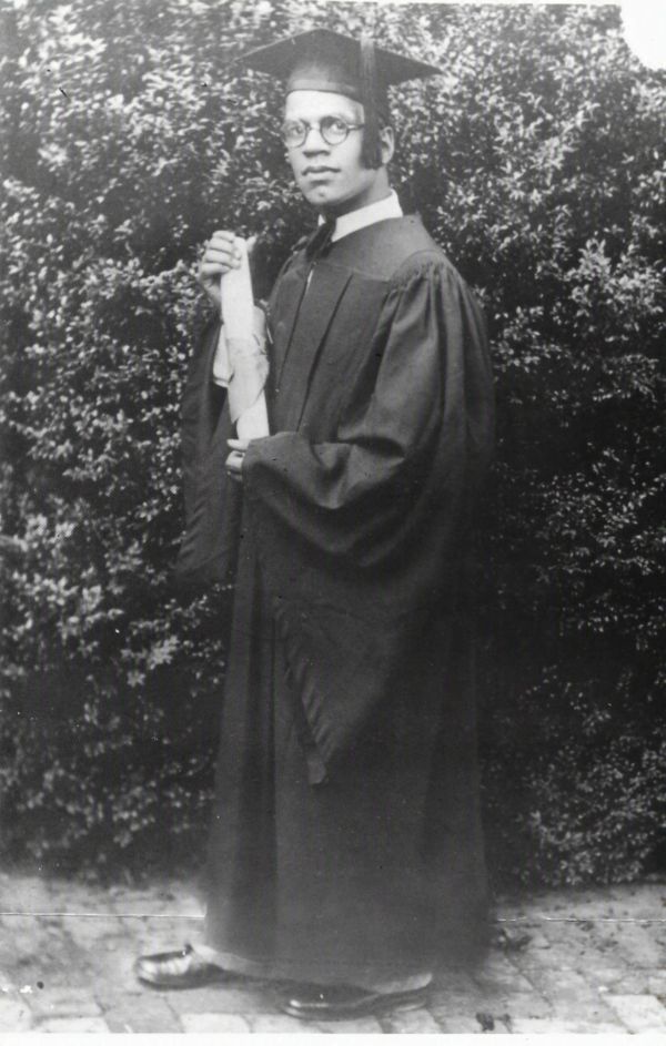 Black and white photo of a man in graduation attire holding a diploma.