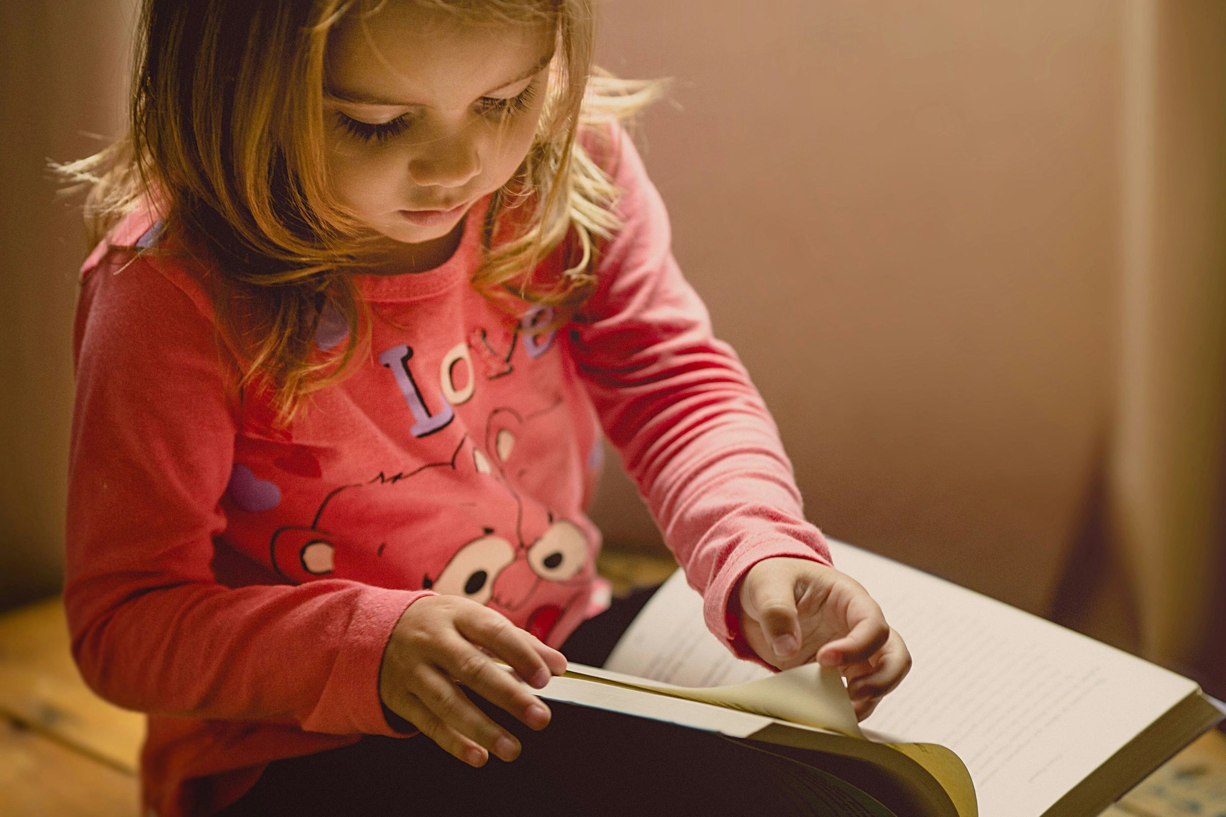 Young girl intently reading a book, turning the page carefully.