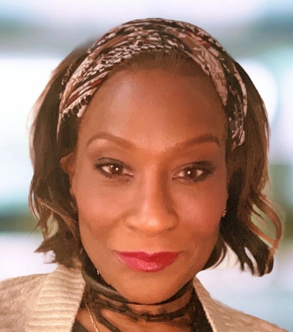 Woman with a patterned headband and red lipstick smiling.