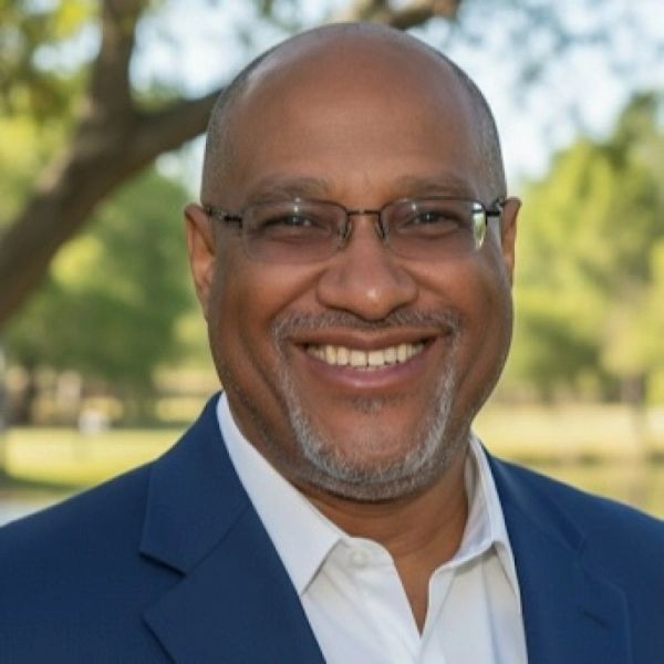 Smiling man in glasses and suit outdoors.