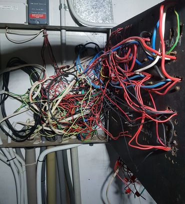 Cables attached to the old, run down & messy switchboard. Wires are everywhere, like a birds nest.  