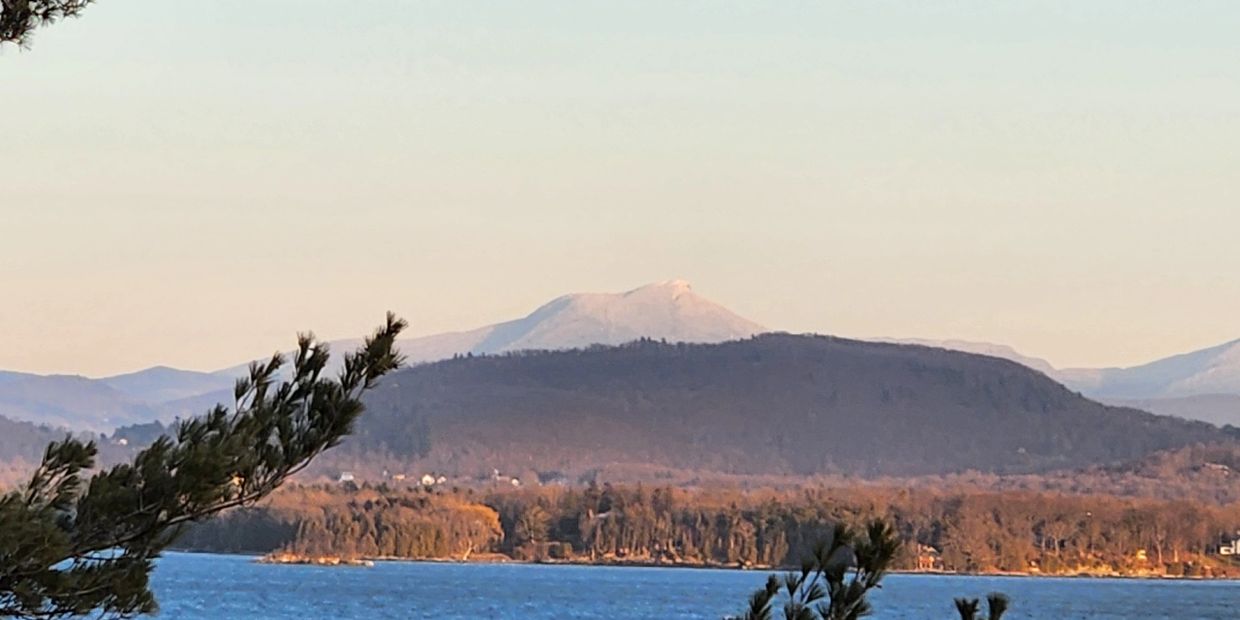 Mountain landscape with a lake and tree branches in foreground during sunset.