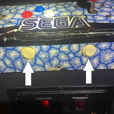 Close-up of a worn SEGA arcade machine panel with yellow buttons and arrows.