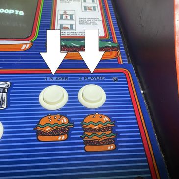 Close-up of a retro arcade game control panel with burger illustrations and player buttons.