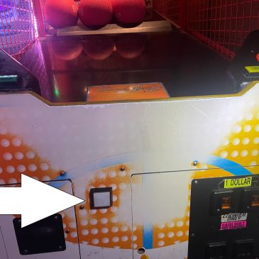 Arcade basketball game coin slot with a white arrow pointing to a button.