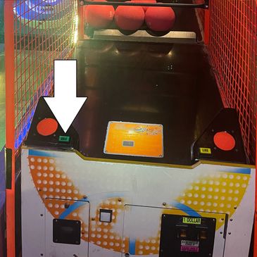 Arcade basketball game with a white arrow pointing to the ticket dispenser.