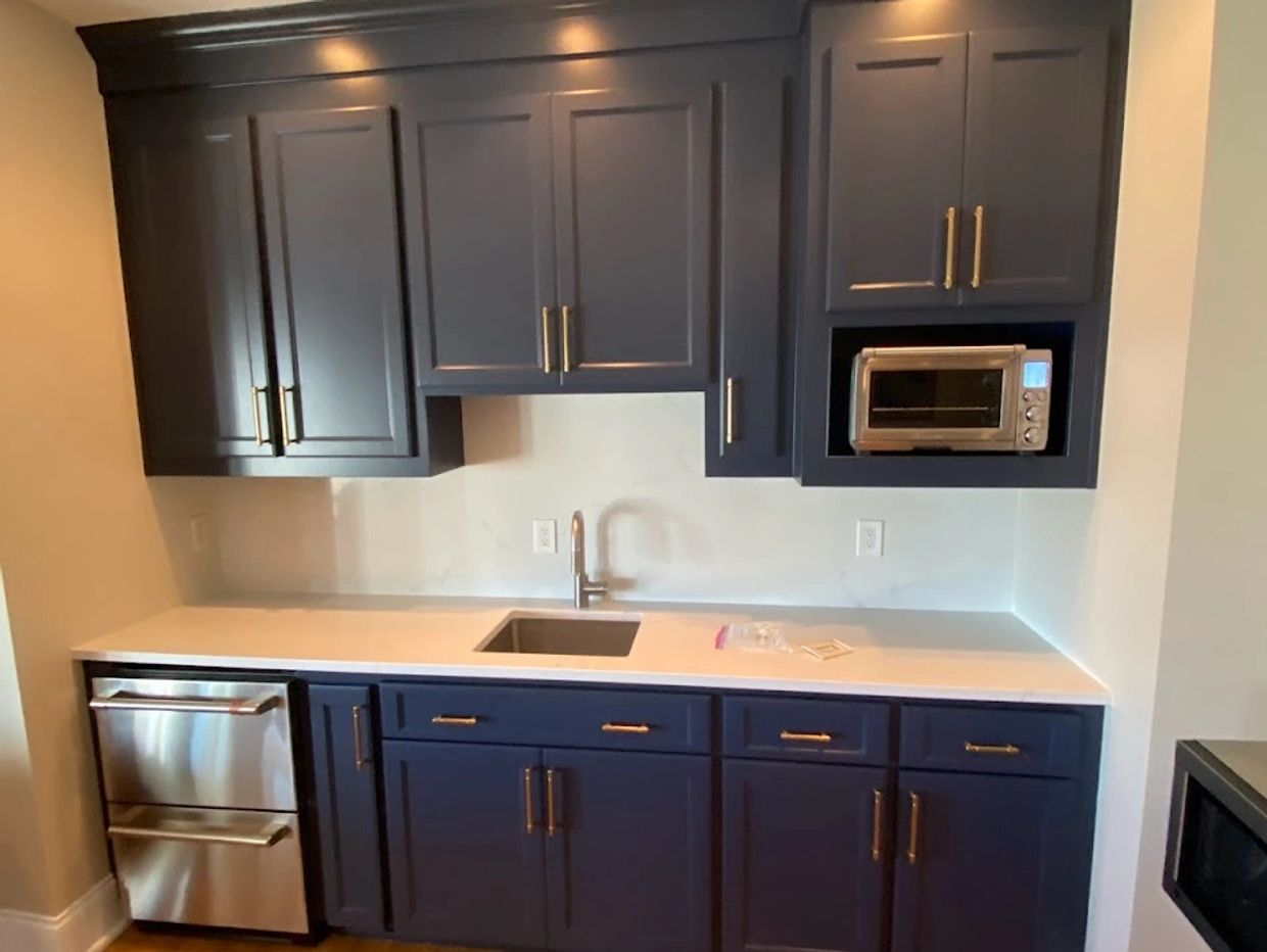 Modern kitchen with navy blue cabinets, white countertop, and stainless steel appliances.