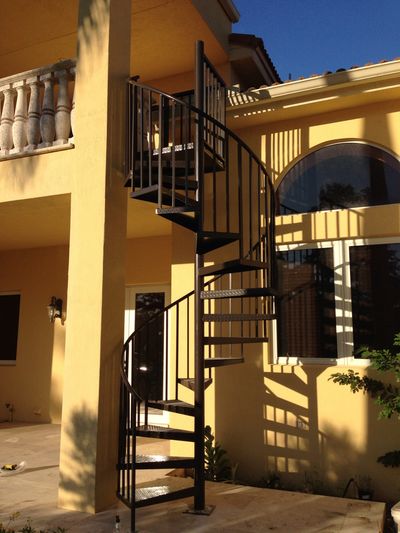 Black metal spiral staircase outside a yellow house with shadows cast on the walls.