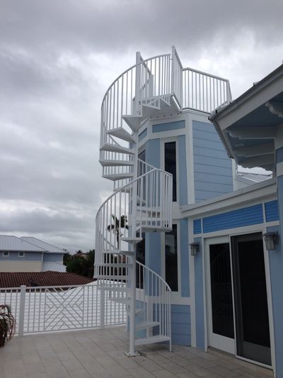White spiral staircase attached to a blue house under cloudy sky.