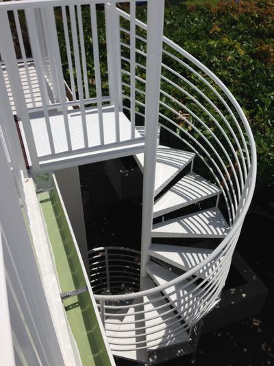 White spiral staircase with metal railings outdoors surrounded by greenery.