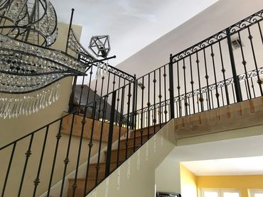 Elegant staircase with ornate black railing and crystal chandelier.