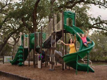 Child sliding down playground slide with adult.