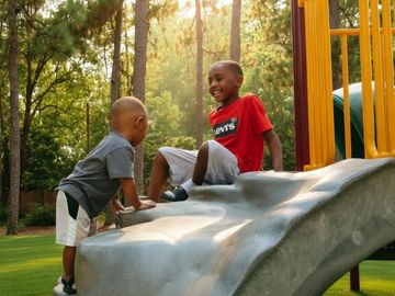 Two boys playing on a slide at the park.