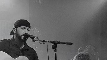 Musician singing and playing guitar on stage in black and white.