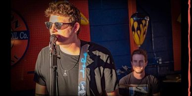 Man singing with a guitarist in the background.