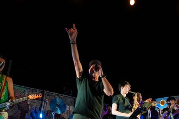 Lead singer passionately performs with band on stage under dim lighting.