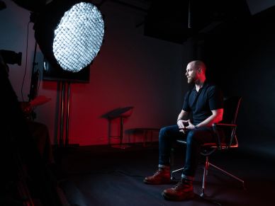 Man sitting in a dark studio illuminated by a large light.