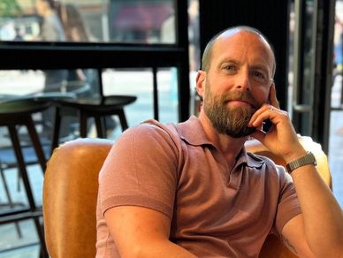 Man with beard sitting in a chair indoors.