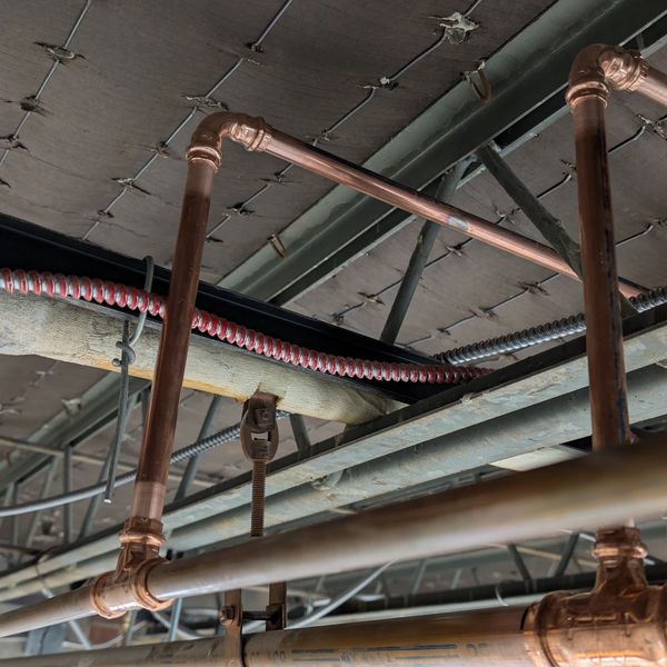 Copper pipes and electrical wiring installed in an industrial ceiling space.