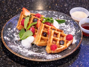 Delicious wafﬂe with strawberries, blueberries and black berries, covered in powdered sugar, bathed 
