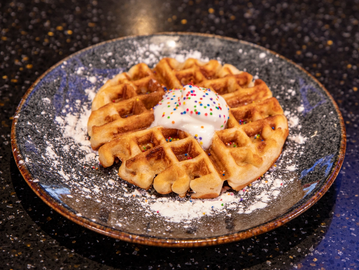 kids waffle Wafﬂe topped with powdered sugar, whipped cream and sprinkles.