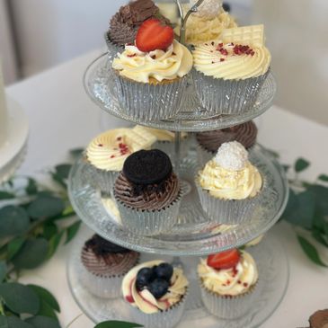 Assorted gourmet cupcakes displayed on a three-tiered glass stand.