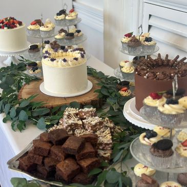 Elegant dessert table with cakes, brownies, and cupcakes decorated with berries and chocolate.
