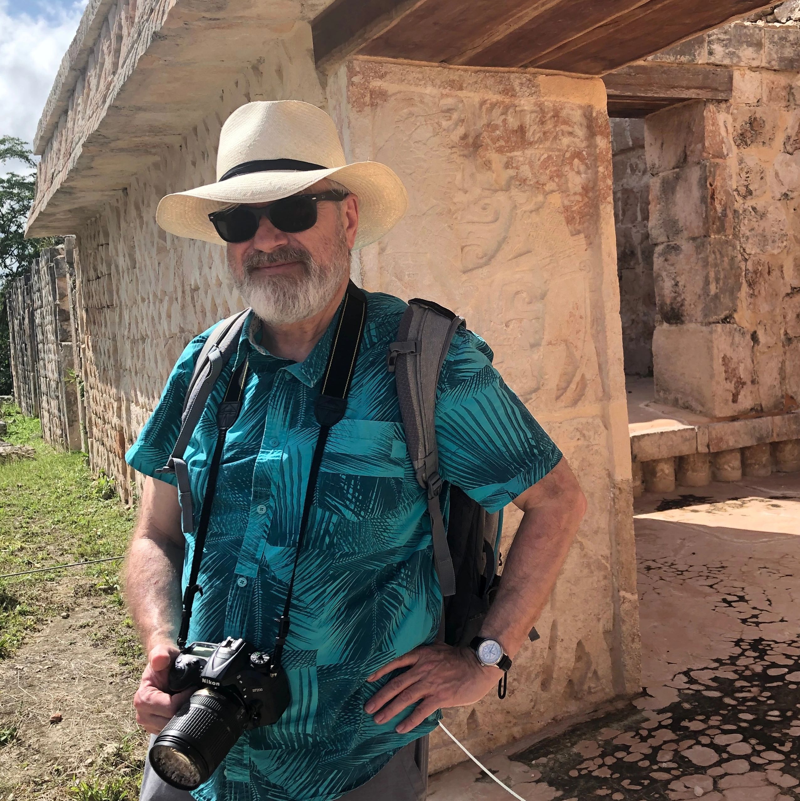 A man in a hat and sunglasses with a camera at an ancient site.