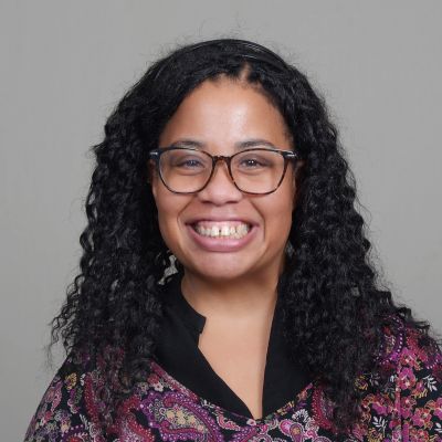 Smiling woman with curly hair and glasses.
