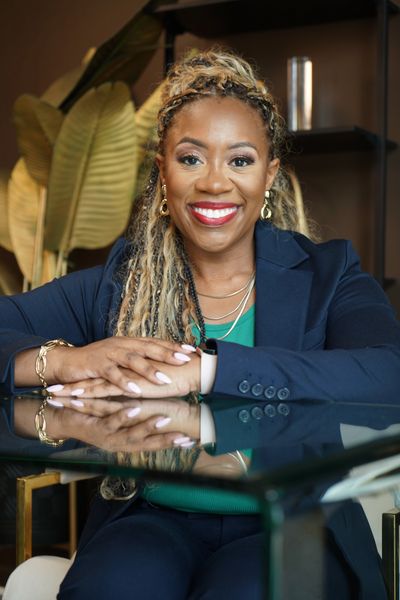 Smiling woman in navy blazer sitting at glass table.