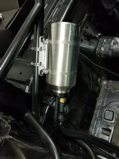 Metallic automotive fluid reservoir mounted inside a vehicle frame.