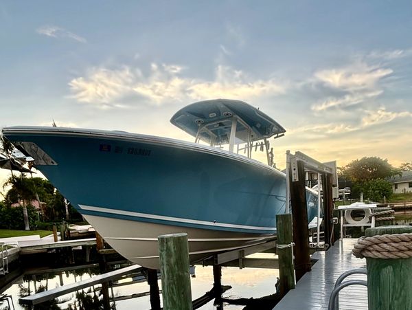 Blue and white boat lifted at a dock during sunset with calm water reflection.