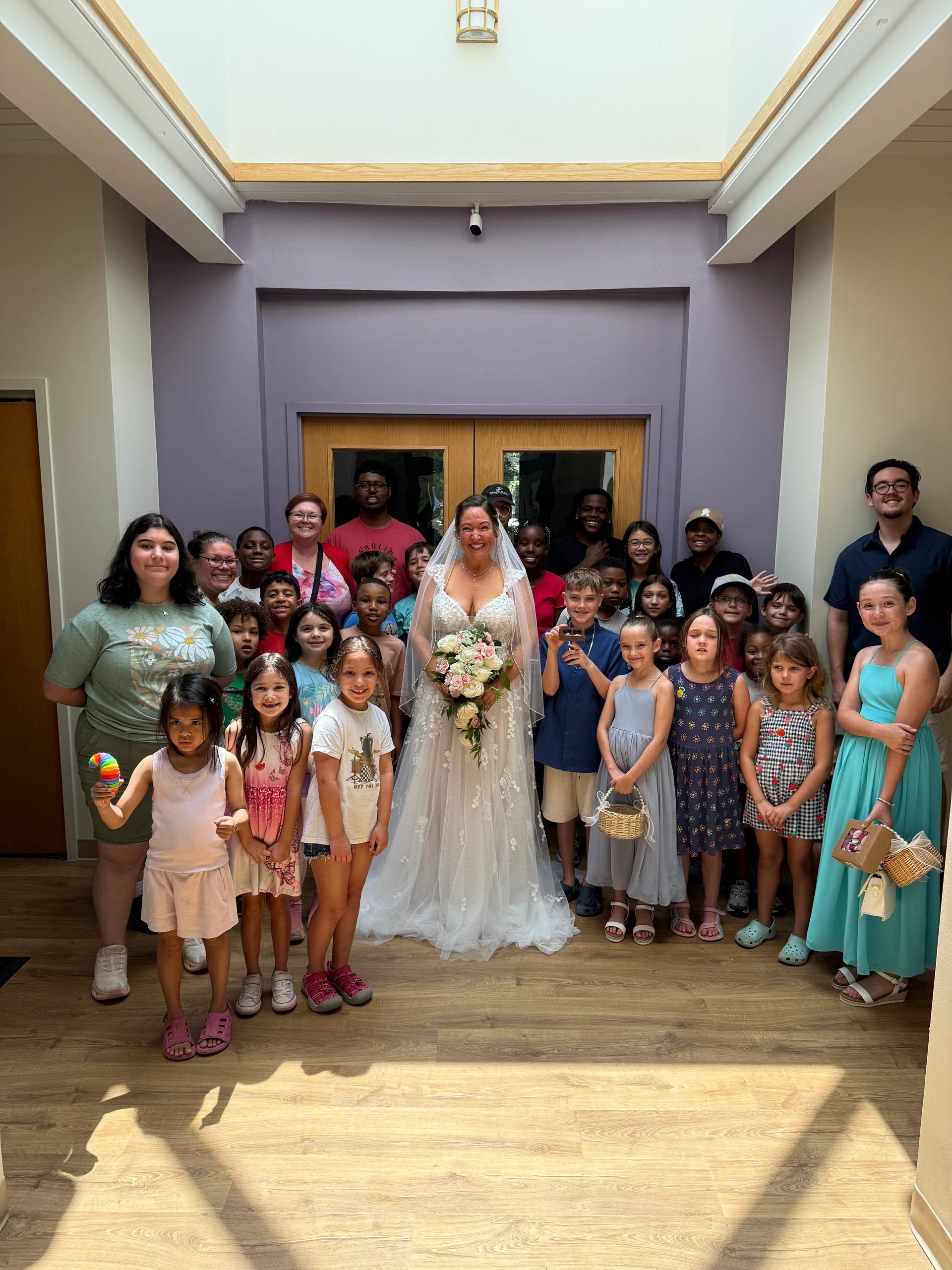 Bride smiling with a large group of adults and children indoors.