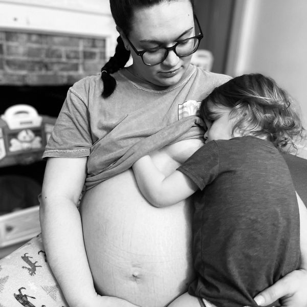 A pregnant woman breastfeeding her toddler in a tender moment.