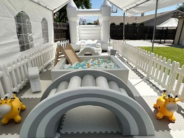 A kids' play area with a ball pit, slide, and inflatable castle in a fenced yard.