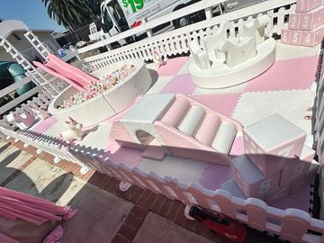 A pink and white soft play area with slides and climbing blocks for toddlers.
