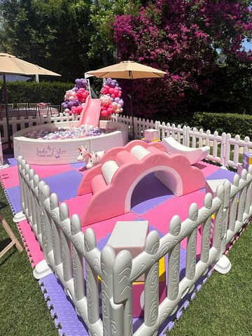 A colorful outdoor kids' play area with a slide, ball pit, and foam mats.