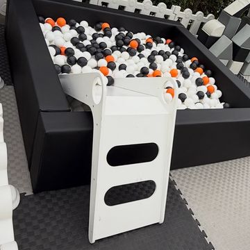 A ball pit filled with black, white, and orange balls and a white ramp attached.