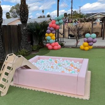 A pink ball pit with a slide and colorful balloon decorations outdoors.