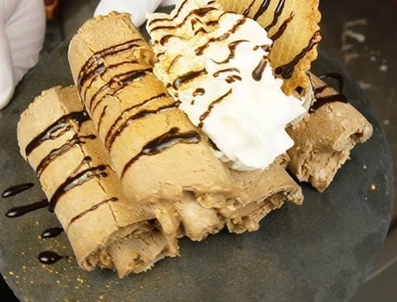 Rolled ice cream with chocolate drizzle and whipped cream.