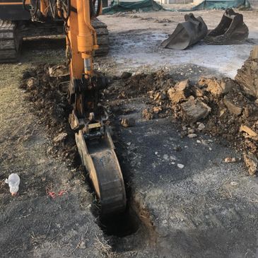 Excavator digging a narrow trench in the ground.