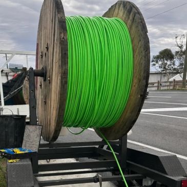 Large wooden spool with green cable on a trailer.