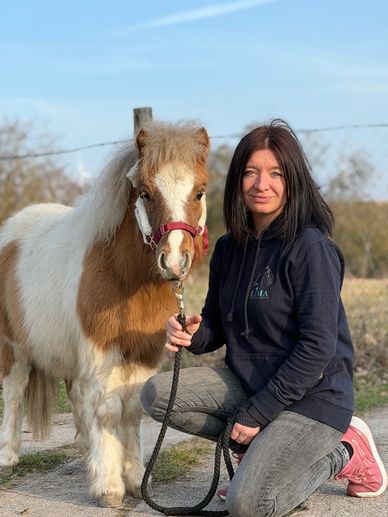 Frau kniet neben einem kleinen Pony im Freien.