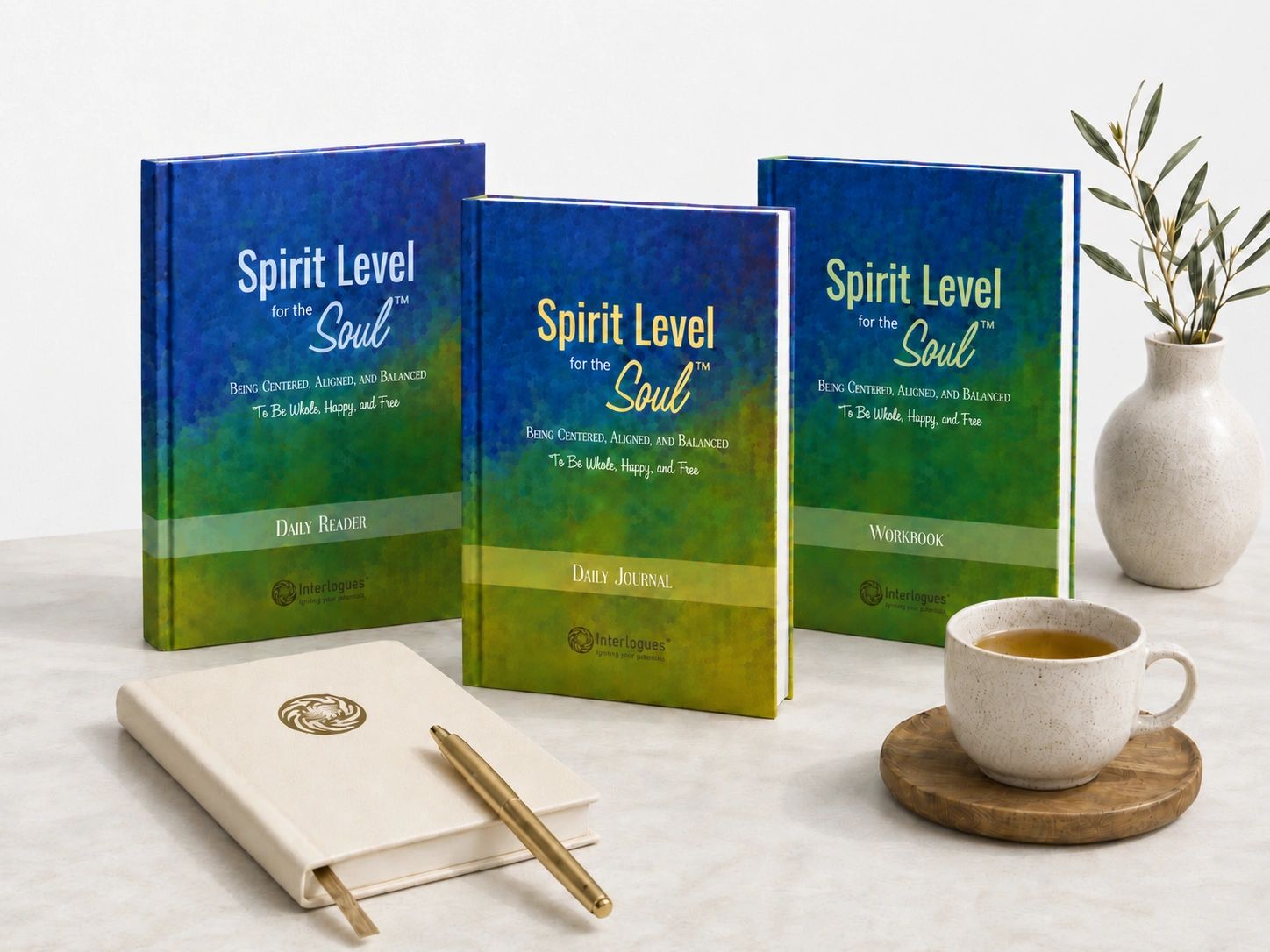 Three 'Spirit Level for the Soul' books with a journal, pen, tea cup, and plant on a white surface.