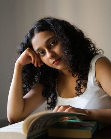 Young woman with curly hair reading a book, resting her head on her hand.