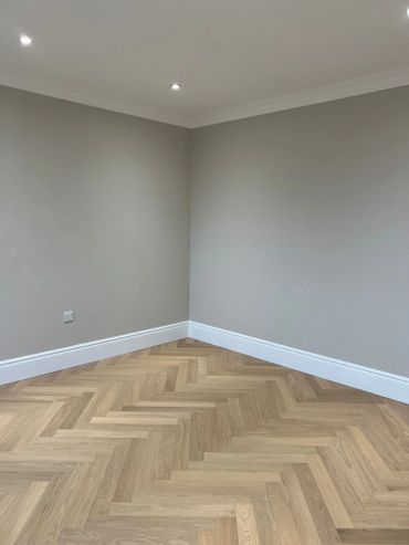 Empty room with herringbone wooden flooring and gray walls.