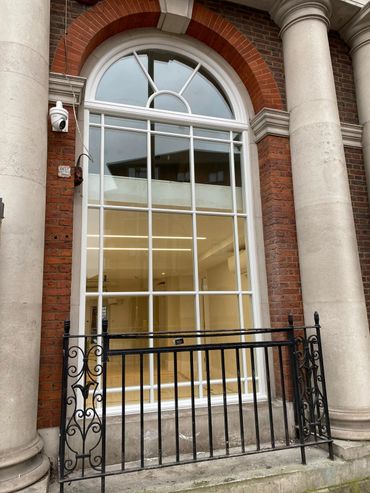 Large arched window with white frame between stone columns and black wrought iron fence.
