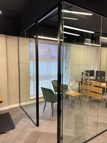 Modern office meeting room with glass walls, green chairs, and wooden furniture.